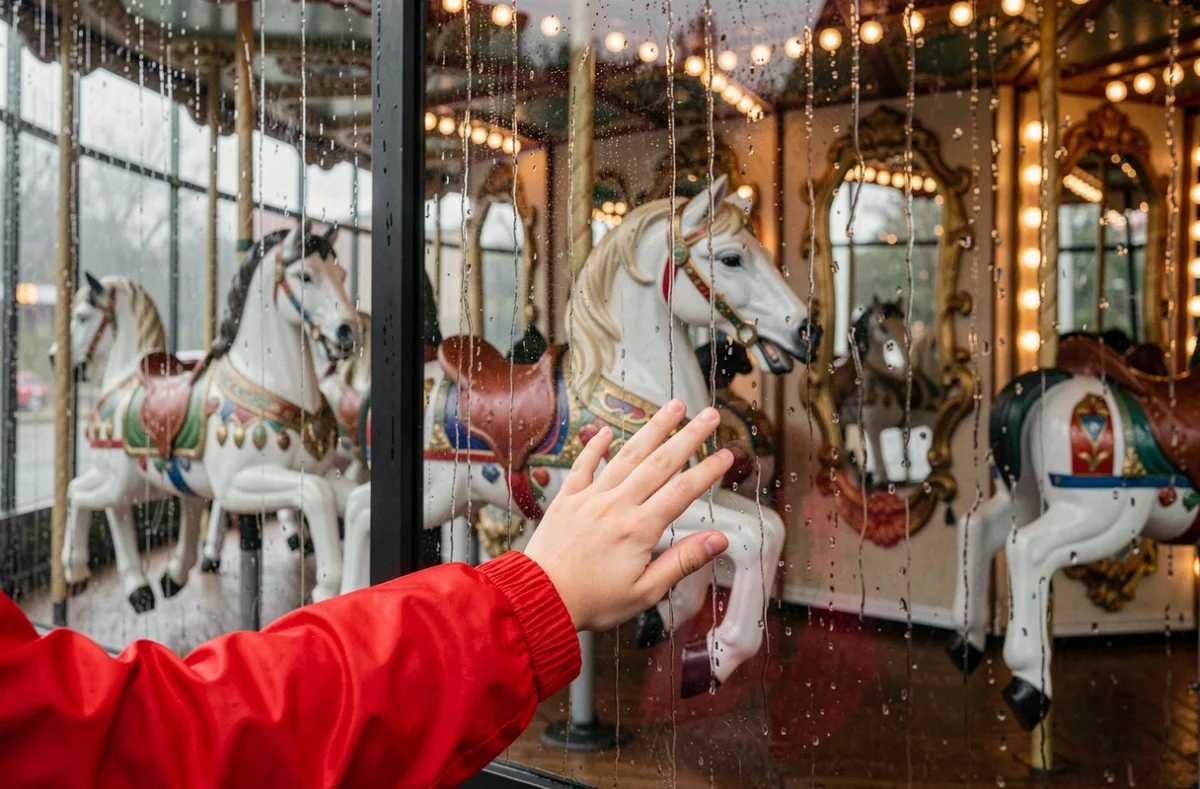 Détail d'un carrousel vintage sous la pluie à la Foire aux Manèges de Lille vu à travers un panneau transparent